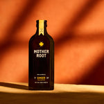 A bottle of Mother Root ginger beverage with a dark label and a star logo, set against a reddish-brown background.