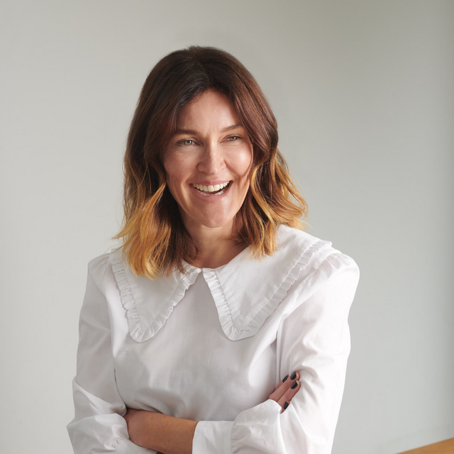 Woman with shoulder-length brown hair in a white blouse smiling confidently, arms crossed against a plain light background.