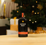 A bottle of Mother Root Marmalade (Limited Edition) sits on a table in front of a festive Christmas tree and gifts.