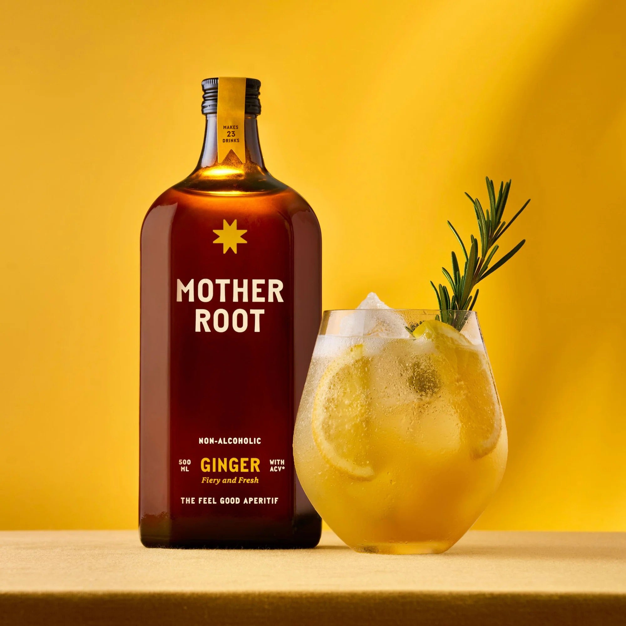 Brown bottle labeled "Mother Root Ginger" beside a glass of ice-filled yellow drink with lemon slices and rosemary on a yellow background.