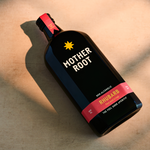 A bottle of Mother Root Rhubarb non-alcoholic aperitif with a vibrant red and yellow label on a light surface.