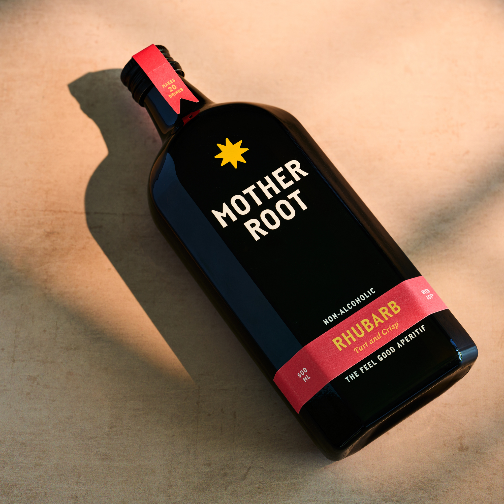 A bottle of Mother Root Rhubarb non-alcoholic aperitif with a vibrant red and yellow label on a light surface.
