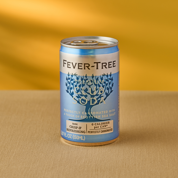 Can of Fever-Tree Premium Club Soda on a beige surface with a yellow background. The label is blue with white text, conveying a crisp, refreshing feel.