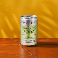 A can of Fever-Tree Mexican Lime Soda on a terracotta tile surface, set against a vibrant yellow background. The tone is fresh and zesty.